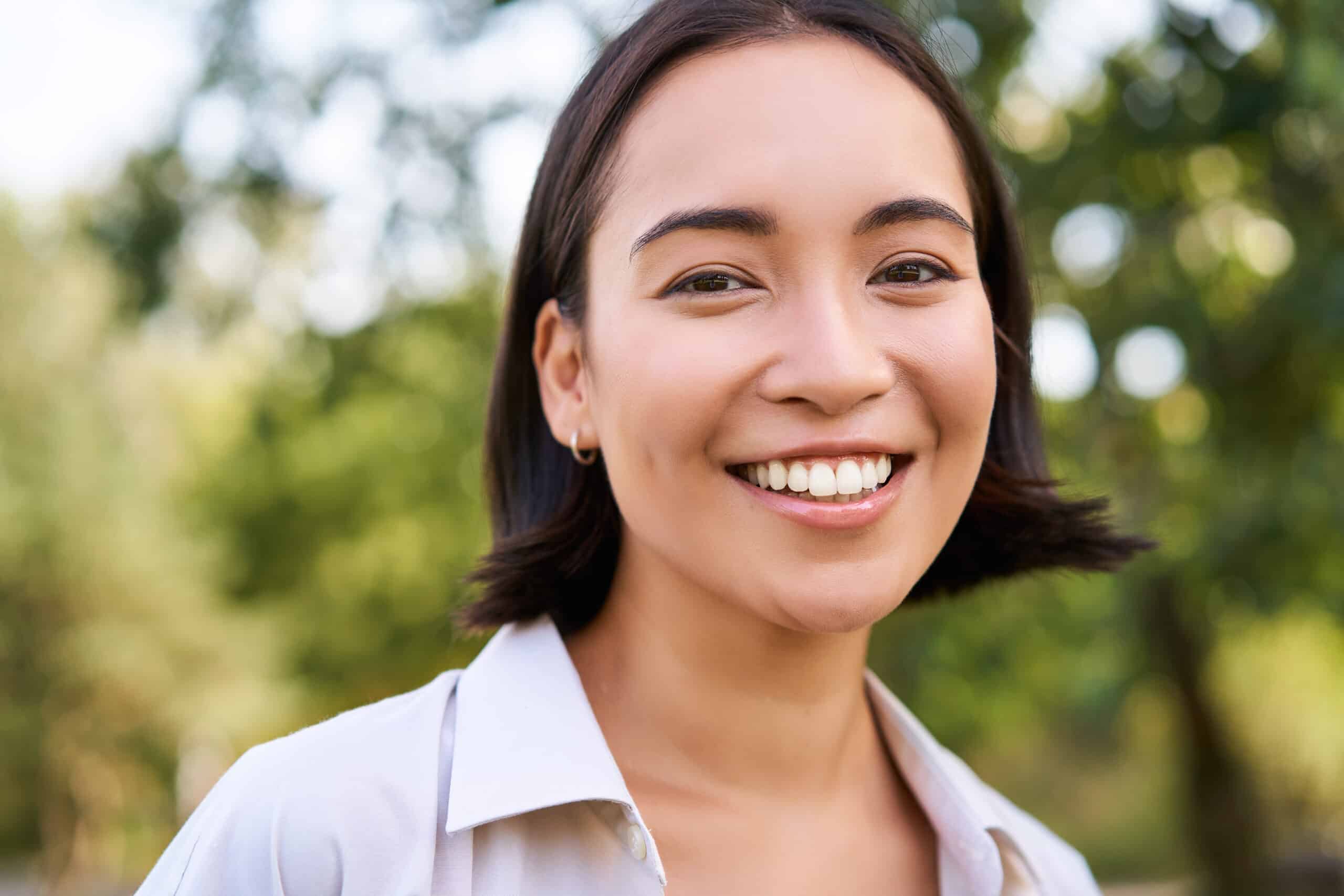 Close up face of asian happy girl, smiling and looking at camera carefree, walking in park.